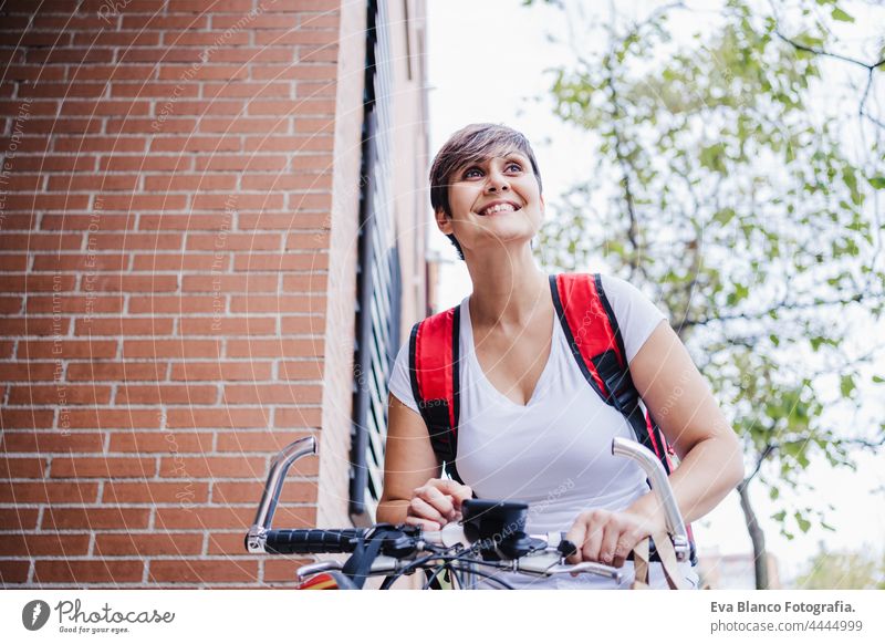 glückliche junge Reiterin mit rotem Rucksack, die eine Pappschachtel mit Lebensmitteln in der Stadt hält. Lieferservice-Konzept. Frau Überprüfung der Bestellung im Mobiltelefon