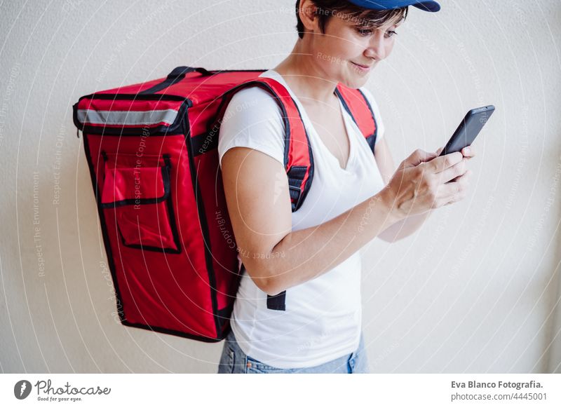 Fahrer Frau trägt roten Rucksack liefern Essen, Überprüfung der Bestellung mit Smartphone, während auf der Straße in der Stadt stehen. Konzept eines Lieferdienstes. Nachhaltiger Transport