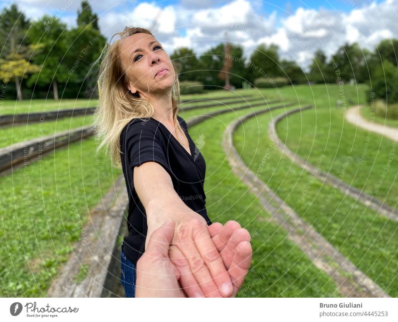 Porträt einer glücklichen weiblichen Person, die lächelt und in die Kamera schaut, draußen in der Natur. Eine blonde Frau hält die Hand eines Mannes.