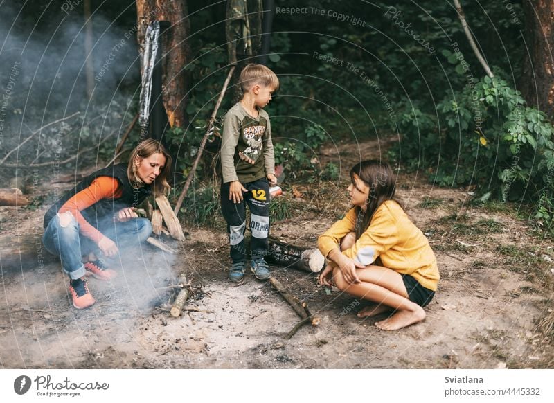 Eine glückliche Familie macht bei einem Ausflug in den Wald ein Feuer. Gemeinsam Zeit verbringen, Familienzeit Mama Tochter Sohn Lagerfeuer Zusammensein