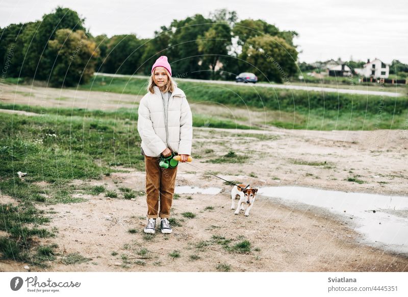 Nettes Teenager-Mädchen, das mit ihrem Hund Jack Russell Terrier an der Leine in einem Feld vor dem Hintergrund eines Kornfelds im Herbst spazieren geht Futter