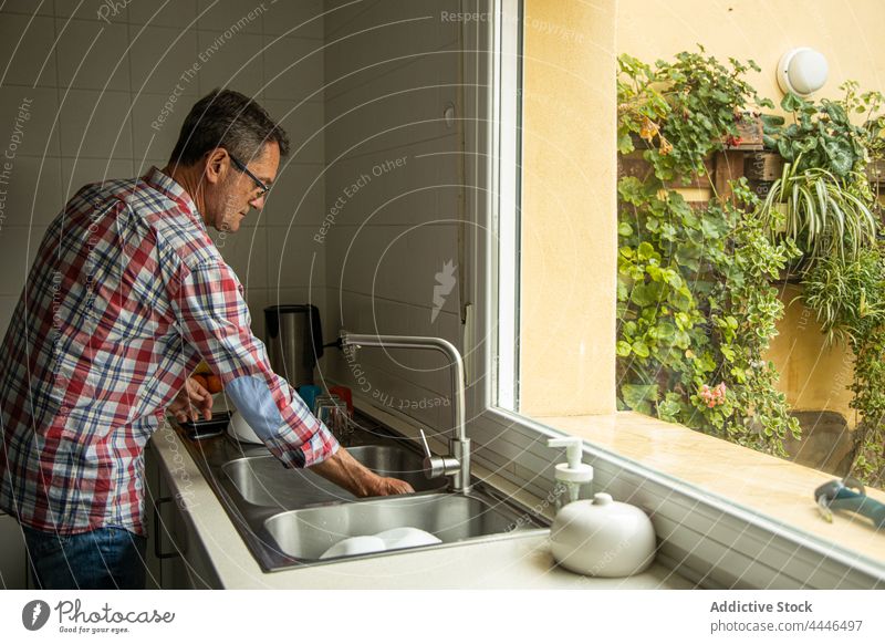 Nachdenklicher Mann beim Abwasch in der Küche zu Hause Waschen Speise nachdenklich Haushalt reinigen Sauberkeit besinnlich Fenster Single stehen Freizeit Seife