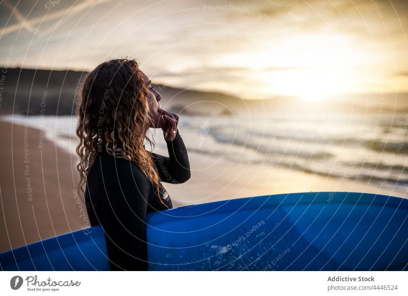 Frau steht pfeifend am Ufer mit Surfbrett und schaut auf das Meer bei Sonnenuntergang Sonnenaufgang Neoprenanzug MEER Sportlerin Spaß Pfeifen nachdenken Wellen