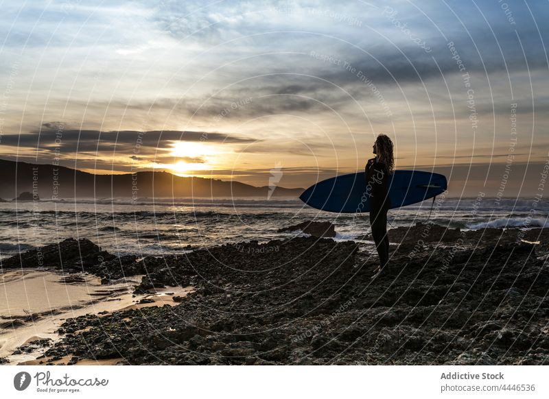 Frau steht am Ufer mit Surfbrett und schaut auf das Meer bei Sonnenuntergang Sonnenaufgang Neoprenanzug MEER Sportlerin Spaß nachdenken Silhouette Wellen