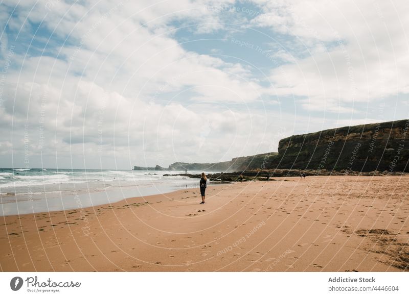 Frau steht in der Nähe des wogenden Meeres am Strand MEER winken Tourist Sommer Urlaub Klippe Blauer Himmel wolkig Spanien Küste Ufer Resort Feiertag Sand