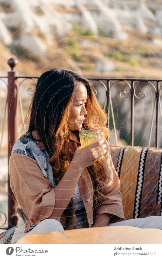 Asiatische Frau trinkt Mojito auf der Terrasse einer Bar schlürfen Stroh Cocktail Glas trinken bewundern Erfrischung Getränk Balkon sitzen Veranda geschmackvoll