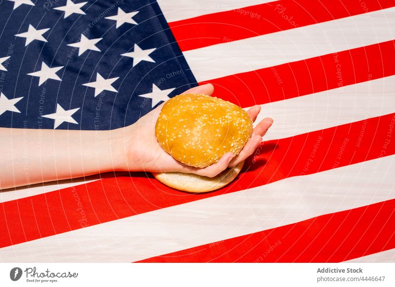 Crop Person mit geschnittenem Brötchen auf amerikanischer Flagge Fahne Hamburger Fastfood USA national Feiertag feiern Konzept Independence Day Demokratie