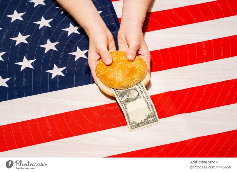 Crop-Person mit geschnittenem Brötchen und Geldschein über USA-Flagge Dollar Banknote Fahne Preis Hamburger Fastfood Konzept Amerikaner Kosten 4. Juli