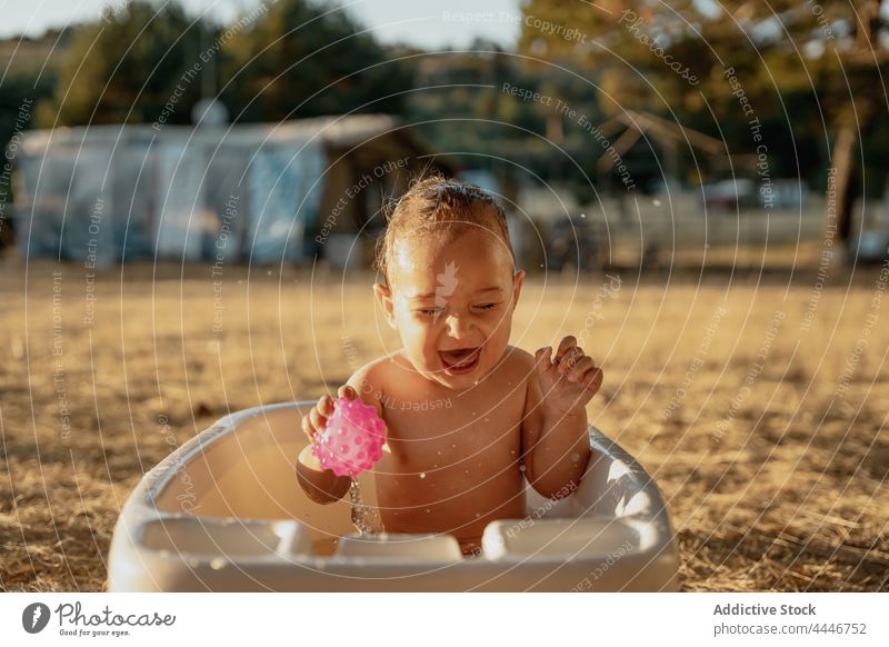 Fröhliches Baby hat Spaß in der kleinen Badewanne spielen Spaß haben heiter sorgenfrei Augen geschlossen Spielzeug Tropfen Landschaft unschuldig Kind Kleinkind