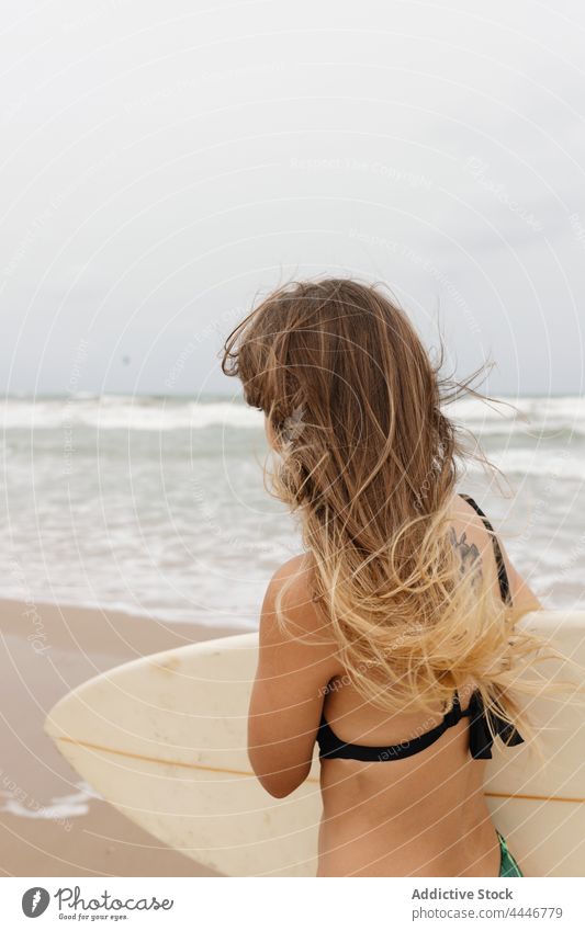 Anonymer Surfer mit Surfbrett am Meeresufer Badeanzug Sport Surfen Körper Küste Himmel Frau stürmisch schaumig sandig Ufer MEER Wetter Beinseil anleinen Gerät
