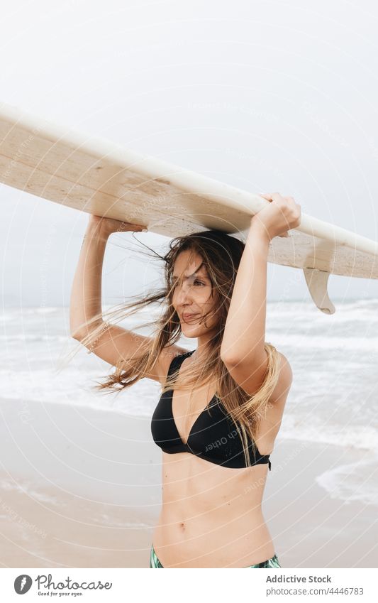 Surfer mit Surfbrett auf dem Kopf am Meeresstrand fliegendes Haar Sport Körper Badebekleidung Surfen genießen Frau Meeresufer Himmel Badeanzug Lächeln Küste