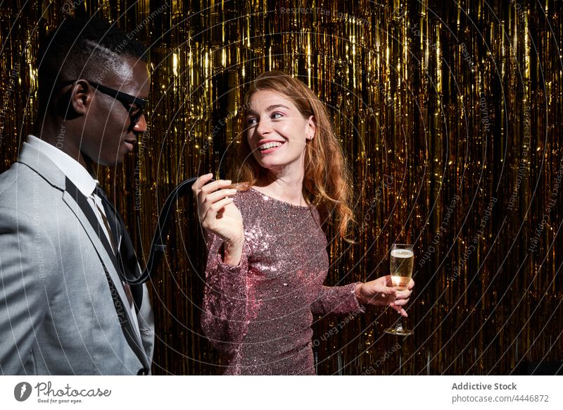 Stilvolles multiethnisches Paar mit Champagner im Gespräch während einer Party Partnerschaft romantisch Neujahr feiern interagieren Feiertag Lächeln Krawatte