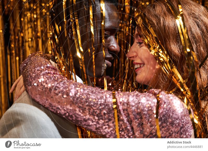 Lächelndes gemischtrassiges Paar mit Lametta, das sich in der Silvesternacht umarmt Umarmen Liebe Partnerschaft Party romantisch Neujahr feiern Porträt Stil