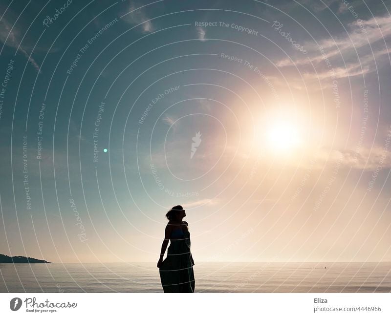 Dunkle Silhouette einer Frau am Meer, die zur leuchtenden Sonne empor blickt Strand Sonnenschein schwarz dunkel Wasser Küste Horizont Sonnenaufgang Sonnenlicht