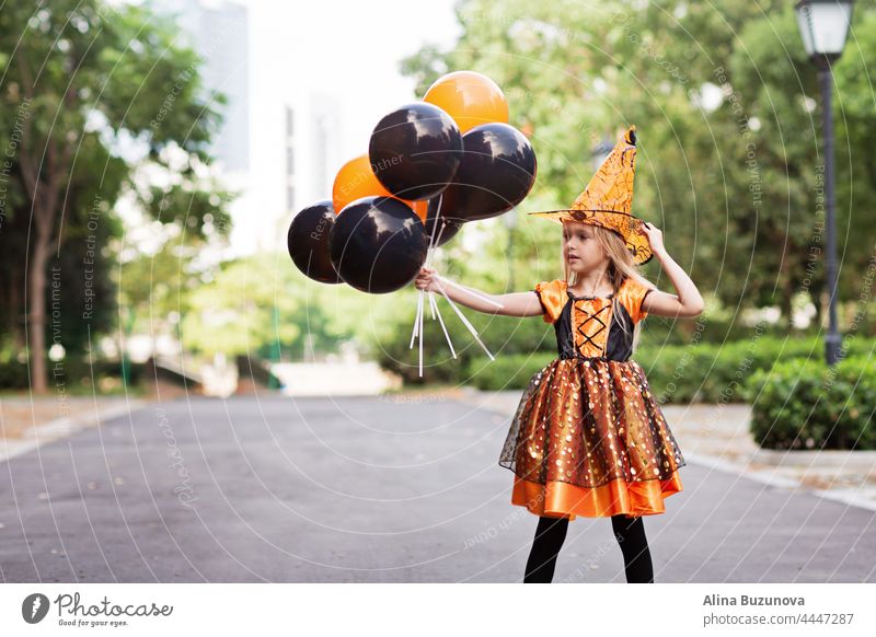 Little Caucasian Girl in Kostüm von denen hält Hand Heißluftballons orange und schwarze Farbe und feiern Halloween Hexe Tracht Hut Kind Mädchen beängstigend