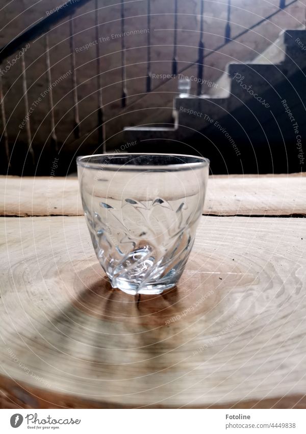 Auf einer Baumscheibe vor einer alten Treppe in einem Lost Place steht ein leeres Glas. Trinkglas Saftglas Maserung Treppengeländer Stufen Holz Metall Licht