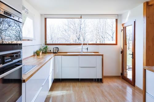 Ecke einer stilvollen Küche mit weißen und gemauerten Wänden, Holzboden und Arbeitsplatten aus Holz Grundbesitz Waschbecken Hocker Geräte Kabinett bequem