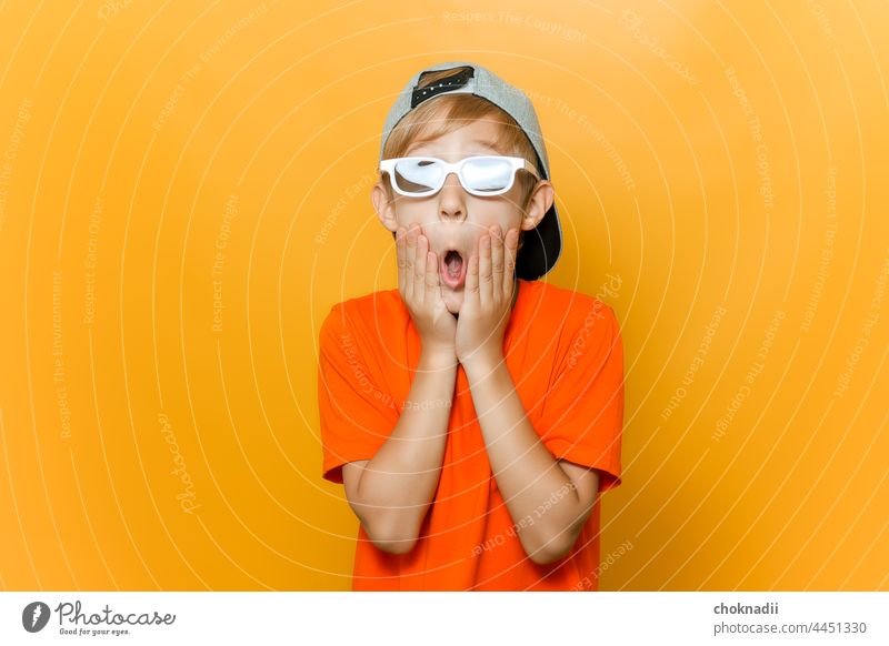 ein Kind mit einer Brille, das sich Filme ansieht, öffnete überrascht den Mund und hielt sich mit den Händen die Wangen Junge Sonnenbrille Mode Gesicht Person