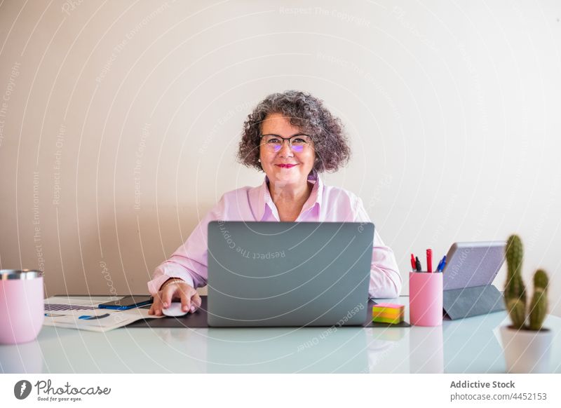 Lächelnder Unternehmer am Schreibtisch mit Laptop im Büro unabhängig selbstbewusst Internet Frau benutzend älter Apparatur Gerät heiter Geschäftsfrau Vorrat
