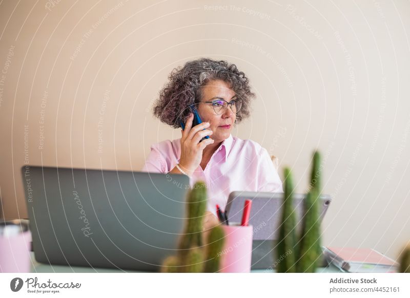 Konzentrierte Geschäftsfrau, die mit ihrem Smartphone vor einem Laptop im Büro spricht Unternehmer sprechen fokussiert Job Internet Frau Arbeitsplatz benutzend