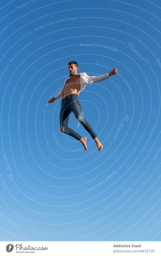Aktive Tänzerin springt gegen blauen Himmel Trick springen aktiv Energie dynamisch furchtlos Blauer Himmel Mann extrem Sprung Barfuß trendy anhaben Jeanshose