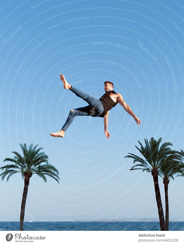 Aktive Tänzerin springt gegen Palme unter blauem Himmel Trick springen aktiv Energie dynamisch furchtlos Blauer Himmel Mann extrem Sprung Barfuß trendy anhaben