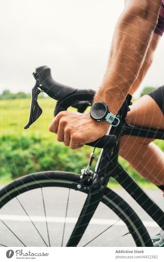 Crop-Radfahrer mit intelligenter Uhr fährt Fahrrad auf der Straße Mitfahrgelegenheit intelligente Uhr Sport Fahrradfahren Training Mann Landschaft kreativ
