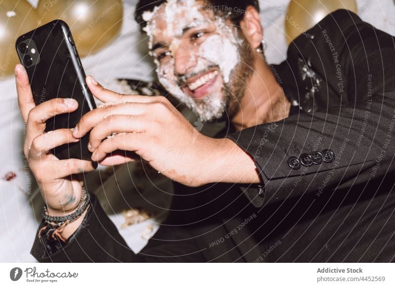 Lächelnder Mann mit Kuchen im Gesicht, der ein Selfie macht Smartphone einschlagen Luftballon benutzend Party Spaß Geburtstag männlich zuschauen positiv Gerät