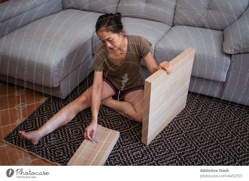 Asiatische Frau beim Zusammenbau eines Tisches auf einem Teppich zu Hause Reittier diy Detailaufnahme schrauben Beine gekreuzt Wohnzimmer heimwärts Tischplatte