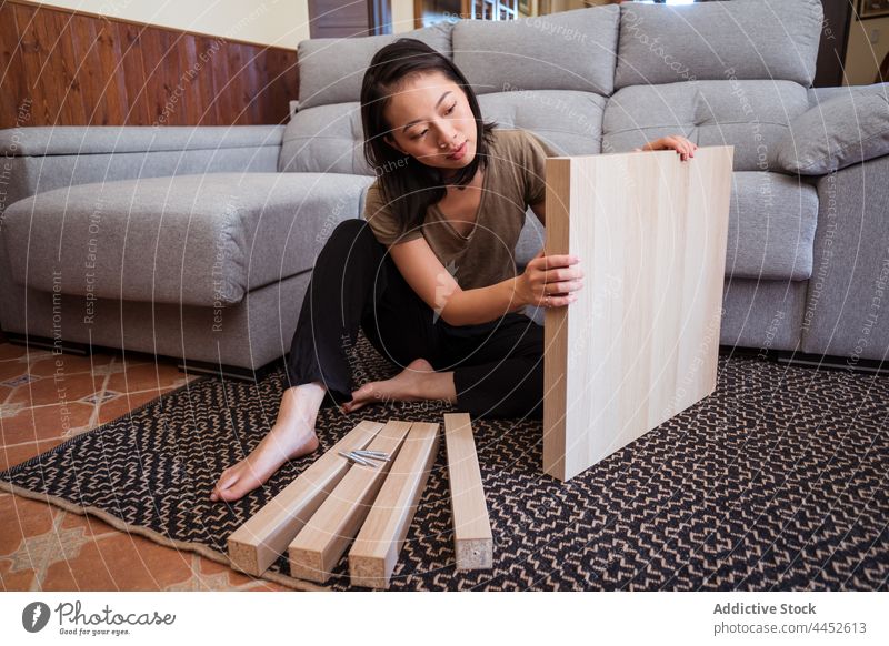 Asiatische Frau baut einen Tisch im Wohnzimmer zusammen versammeln achtsam Detailaufnahme diy Teppich Ornament Sofa heimwärts Raum Fokus Material Barfuß