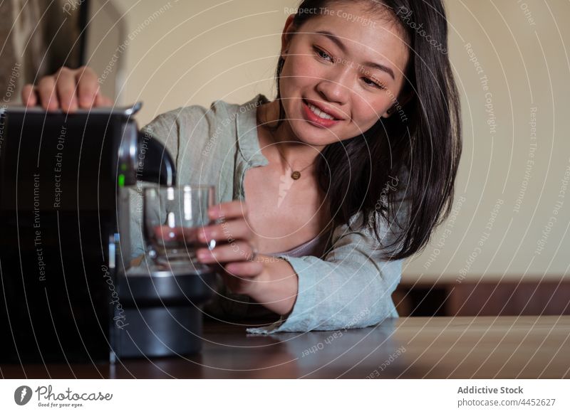 Asiatische Frau bereitet Heißgetränk in Kaffeemaschine zu eingießen Glas Getränk Kapsel nachdenken heimwärts professionell Einwegartikel Einmalgebrauch Lächeln