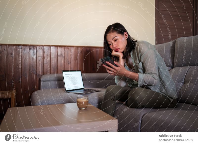 Asiatische Frau mit Milchkaffee berührt den Bildschirm ihres Smartphones Latte Touchscreen Surfen Internet Kaffee Heißgetränk heimwärts benutzend Apparatur