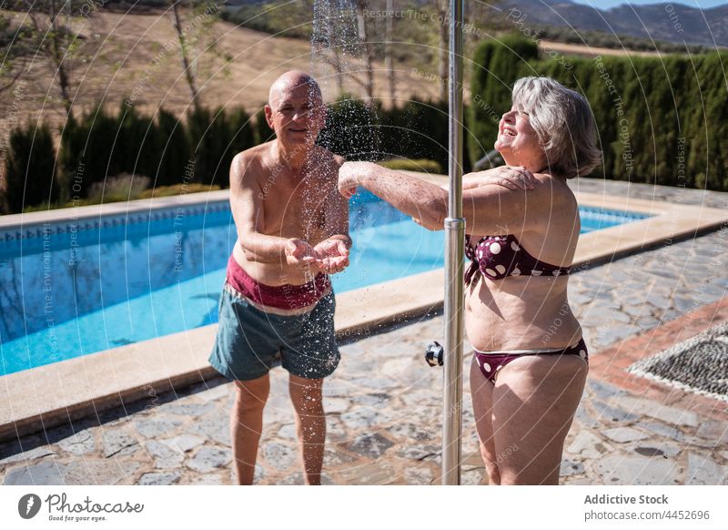 Lächelndes älteres Paar beim Duschen am Pool Senior Waschen aktualisieren genießen Beckenrand Wasser Vergnügen Ehemann Mann Frau Ehefrau Zusammensein positiv