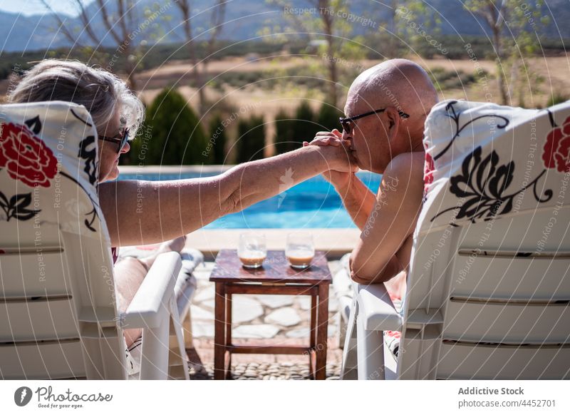 Mann küsst die Hand seiner Frau beim Chillen am Pool Paar Liebe Kuss Senior Liege Beckenrand sanft romantisch Bonden Kälte Ehefrau Ehemann Rentnerin Sommer