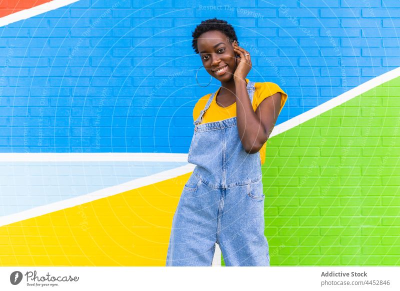 Energetische schwarze Frau steht gegen bunte Wand positiv farbenfroh Aktion Glück Energie sich[Akk] bewegen Spaß Optimist lässig sorgenfrei Freude Vergnügen