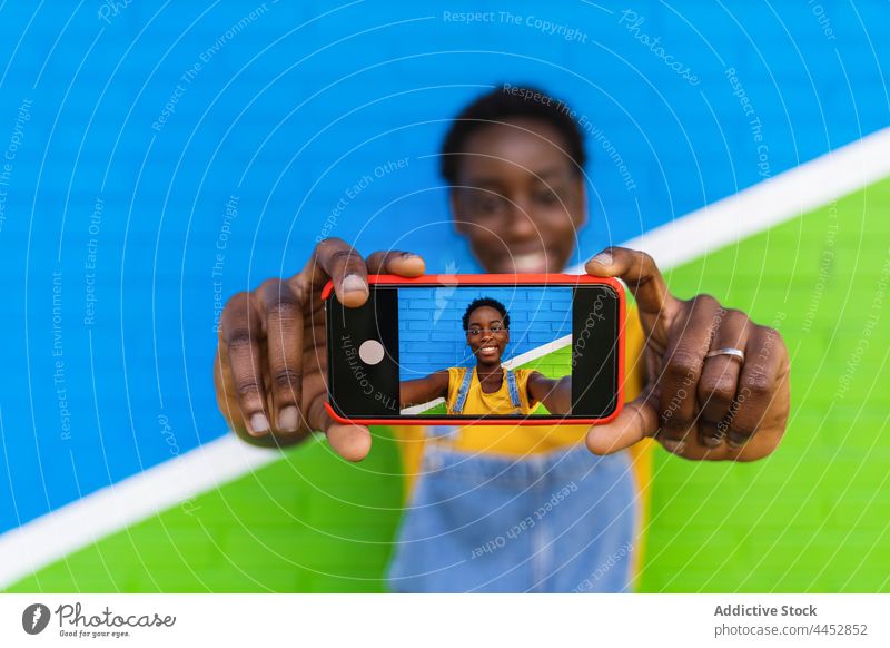 Lächelnde schwarze Frau, die ein Selfie mit ihrem Smartphone macht benutzend froh genießen farbenfroh einfangen Foto Bildschirm Gerät Glück Selbstportrait