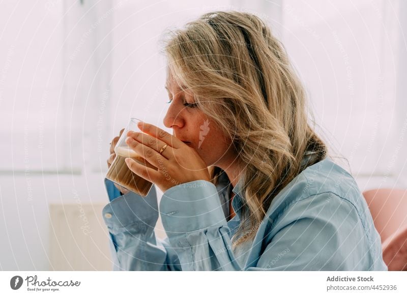 Verträumte Frau genießt köstlichen Milchkaffee zu Hause trinken Latte Kaffee Heißgetränk Getränk reflektierend natürlich Aroma heimwärts schäumen aromatisch
