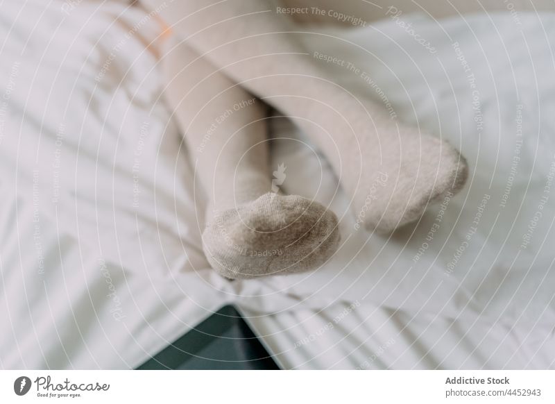 Crop-Frau, die sich zu Hause auf dem Bett an ihr Smartphone lehnt Beine gekreuzt Kniestrumpf reflektieren schwarzer Bildschirm Kälte ungemacht heimwärts