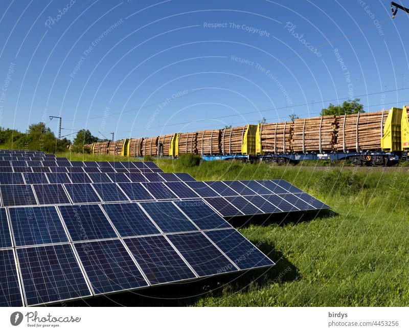Freiland - Photovoltaikanlage . Im Hintergrund fährt ein mit Baumstämmen beladener Güterzug vorbei photovoltaik freilandphotovoltaikanlage grüner Strom
