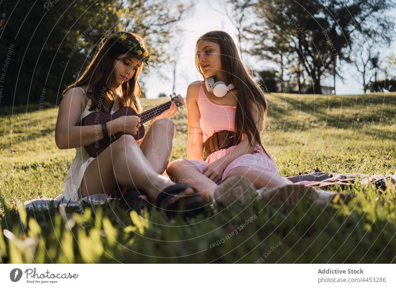 Musiker spielt Ukulele gegen Freundin mit Headset im Park Teenager spielen Kunst klassisch Melodie Zeit verbringen Freundschaft Klang Blume Totenkranz