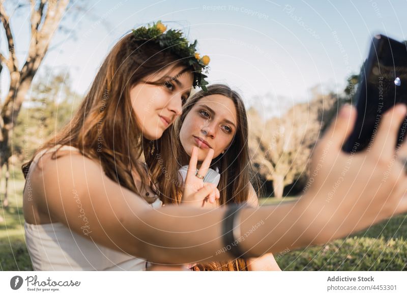 Freundinnen zeigen eine Friedensgeste, während sie ein Selfie mit dem Smartphone machen zwei Finger Gedächtnis Moment Zeit verbringen Park benutzend Apparatur