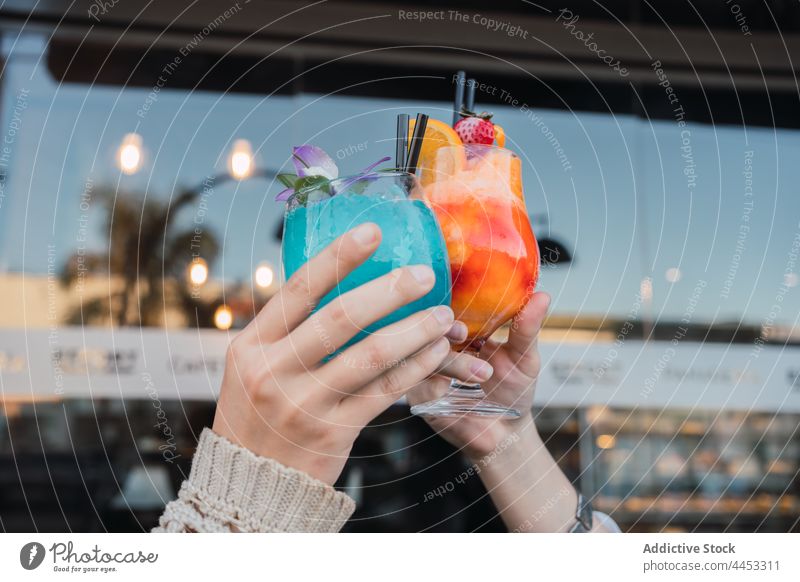Anonyme Freundinnen stoßen in einem Straßencafé mit Cocktails an Glas Klirren Erfrischung trinken Getränk Zeit verbringen Café interagieren Pflanze Topf Inhalt