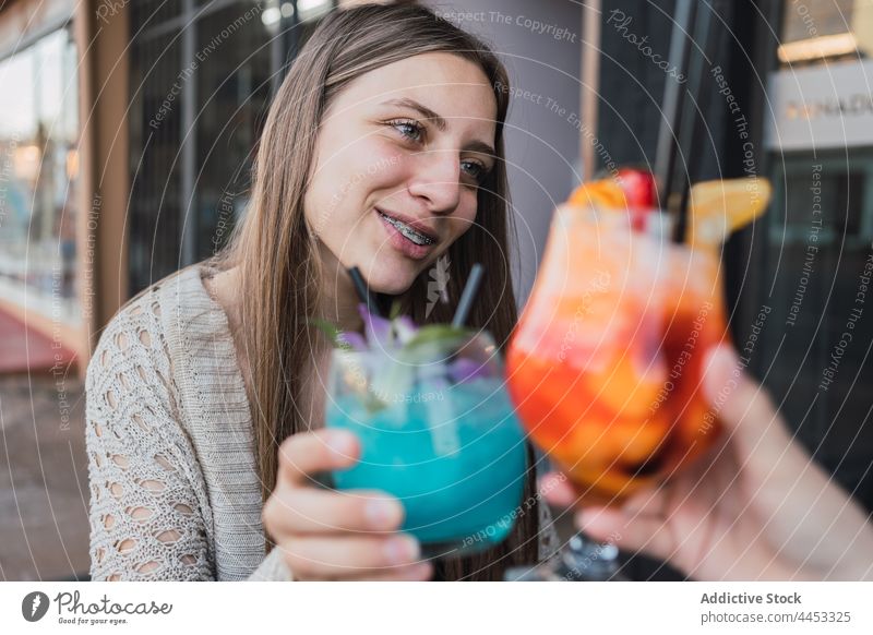 Lächelnde Freundinnen stoßen in einem Straßencafé mit Cocktails an Glas Klirren Erfrischung trinken Getränk Zeit verbringen Café heiter interagieren Topf Inhalt