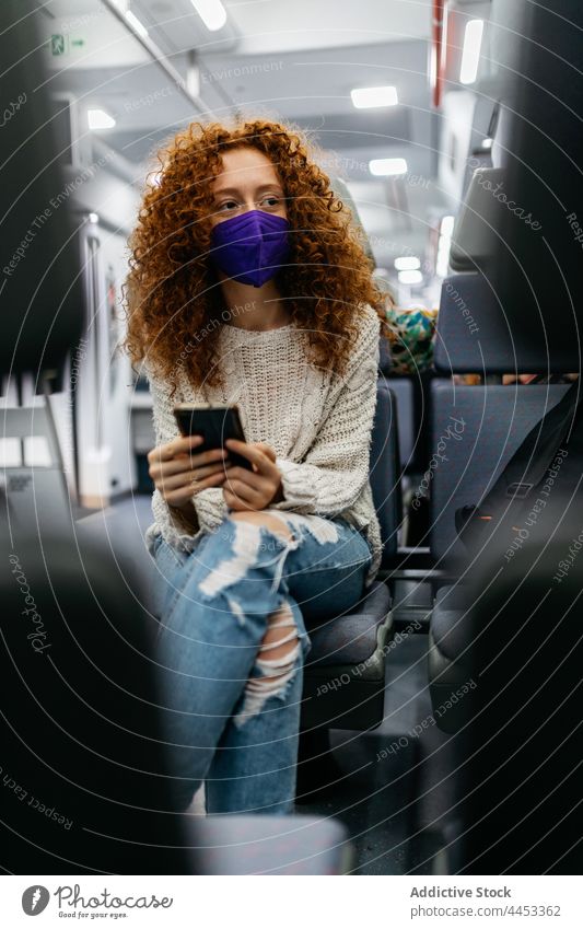 Fahrgast mit Textilmaske, der im Zug mit seinem Smartphone chattet Passagier Mundschutz Surfen Internet neue Normale Gesundheitswesen Frau benutzend Apparatur