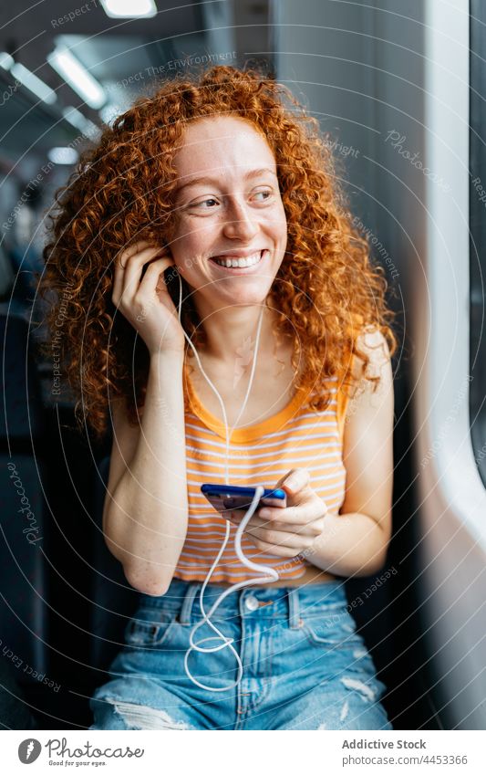 Lächelnder Passagier mit Smartphone, der über Kopfhörer Musik hört zuhören offen Arbeitsweg Frau Zug benutzend Apparatur reisen Internet Inhalt heiter genießen