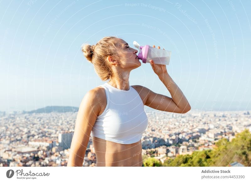 Fitte Sportlerin trinkt Wasser unter hellem Himmel in sonniger Stadt Athlet trinken Hydrat durstig Hand an der Hüfte sportlich Körper Frau Großstadt Pause