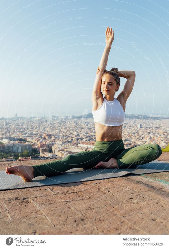 Frau streckt Arm auf Yogamatte in der Stadt Dehnung Gesunder Lebensstil Arme Wellness Vitalität Dachterrasse Blauer Himmel Großstadt Pose üben Wohlbefinden