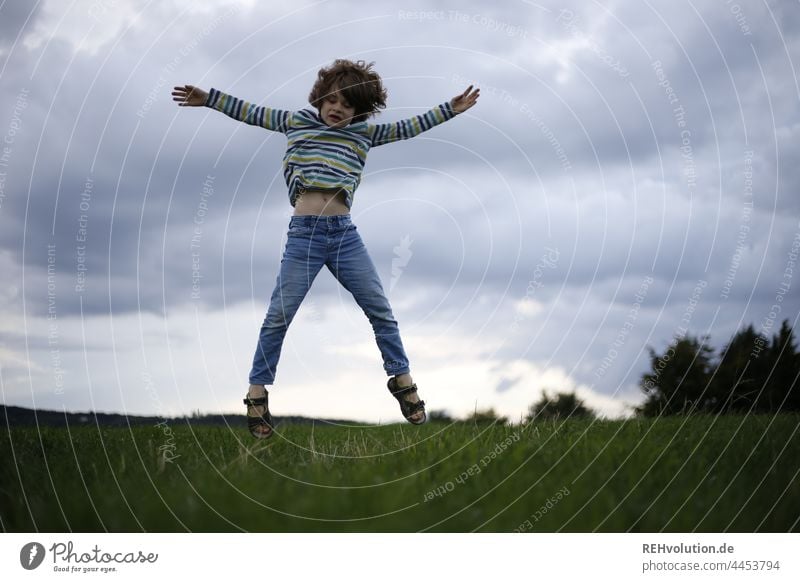 Kind springt auf einer Wiese Kindheit Junge sportlich springen hoch Dynamisch sprung Bewegung aktiv Sport Bäume Freude hüpfen Außenaufnahme Freizeit & Hobby Tag