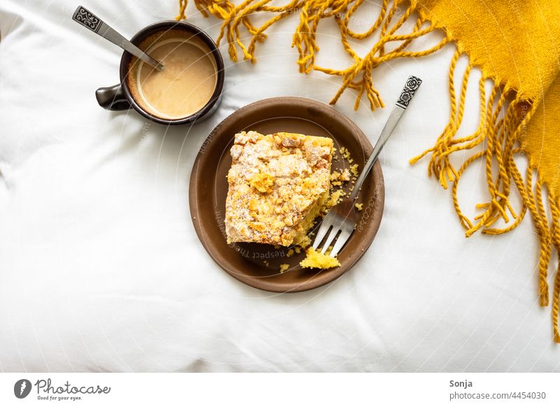 Ein Stück Apfelkuchen auf einem Teller und eine Tasse Kaffee auf einer weißen Bettdecke. Ansicht von oben. Frühstück Kaffeepause Morgen Hygge Koffein Dessert