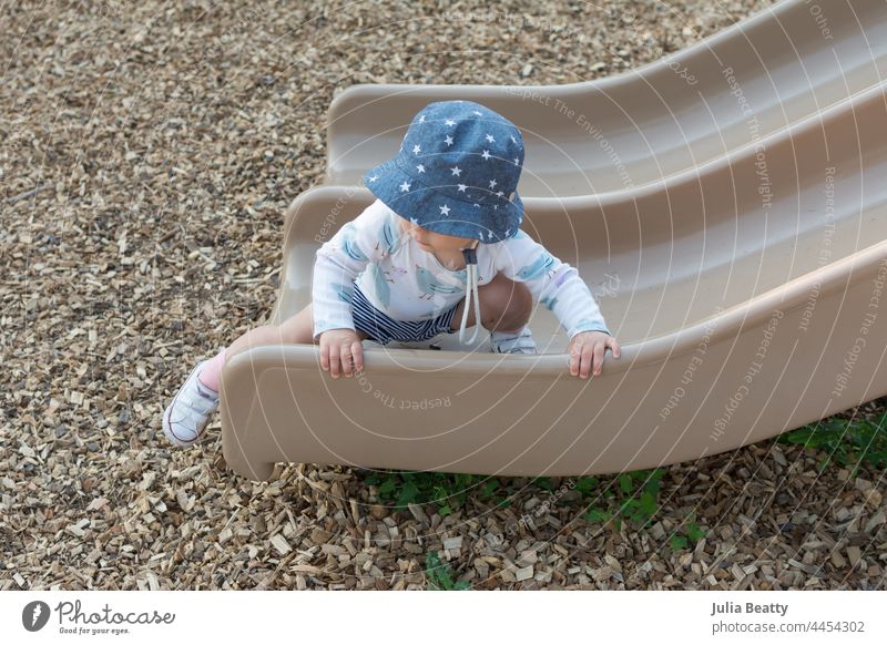 Ein 15 Monate altes Kleinkind, das sich auf dem Spielplatz bewegt; ein Kind, das auf einer Rutsche krabbelt und dabei beide Hände zum Greifen und Ziehen benutzt